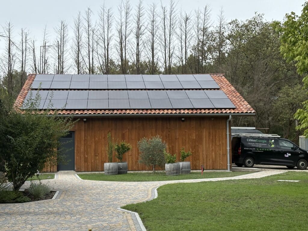 Bâtiment bois avec toit tuilé et panneaux solaires. Camionnette CélécoEnergie (électricité, photovoltaïque, 40430 CALLEN, Tél. 06 25 75 92 77).